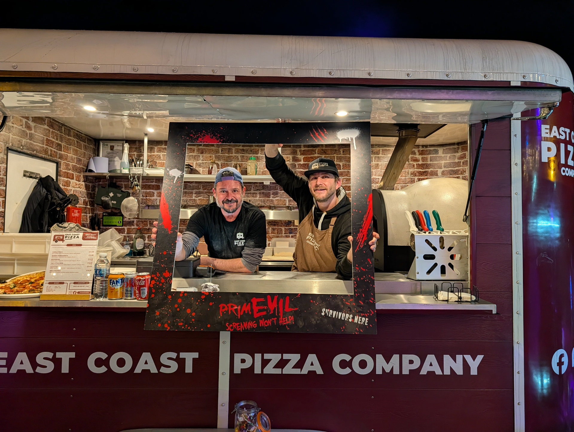 Chris and a teammate inside the Nag Box holding a PrimEvil photo frame at a Halloween event