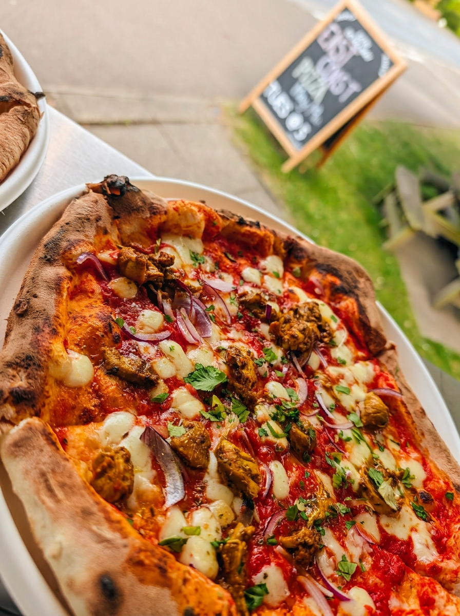 Chicken tikka pizza with red onion and coriander served on a plate beside the trailer