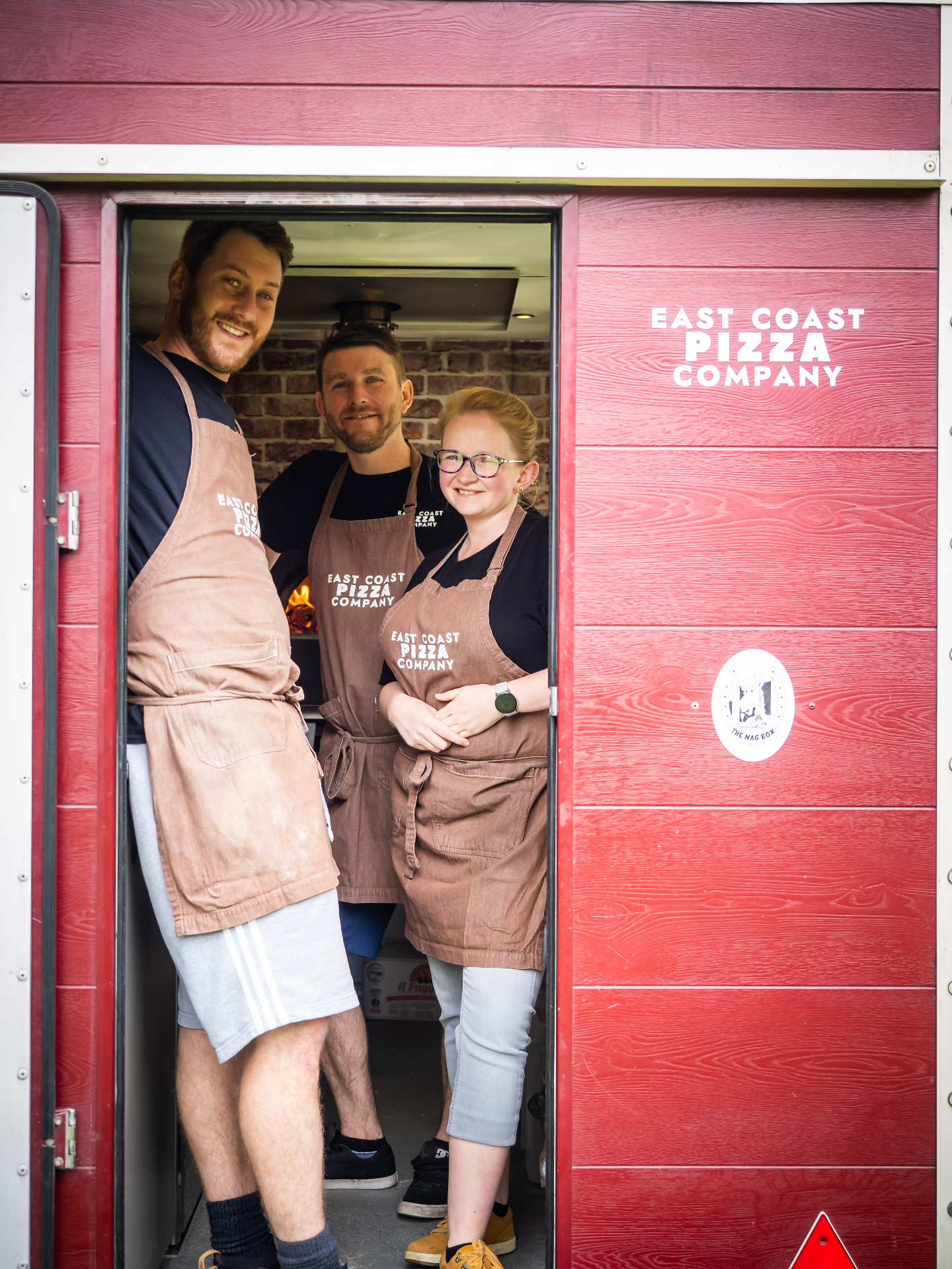 The East Coast Pizza team smiling in the doorway of the Nag Box trailer