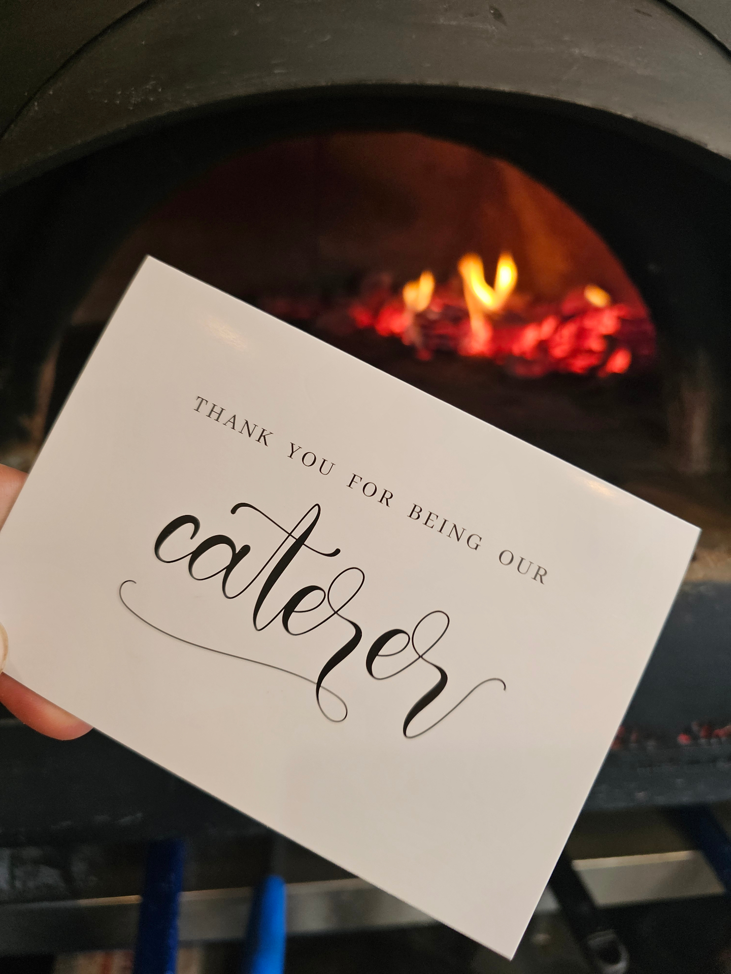 A thank-you card from a wedding couple held in front of the wood-fired oven