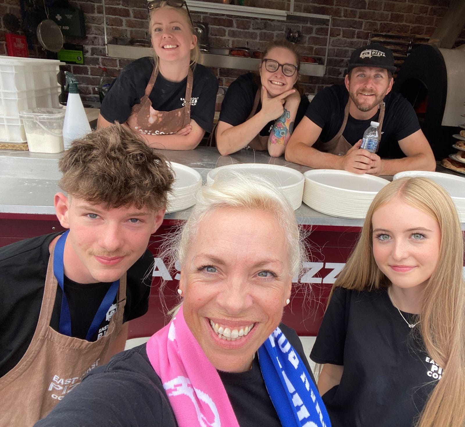 The East Coast Pizza team and family in a selfie behind the service counter at an event