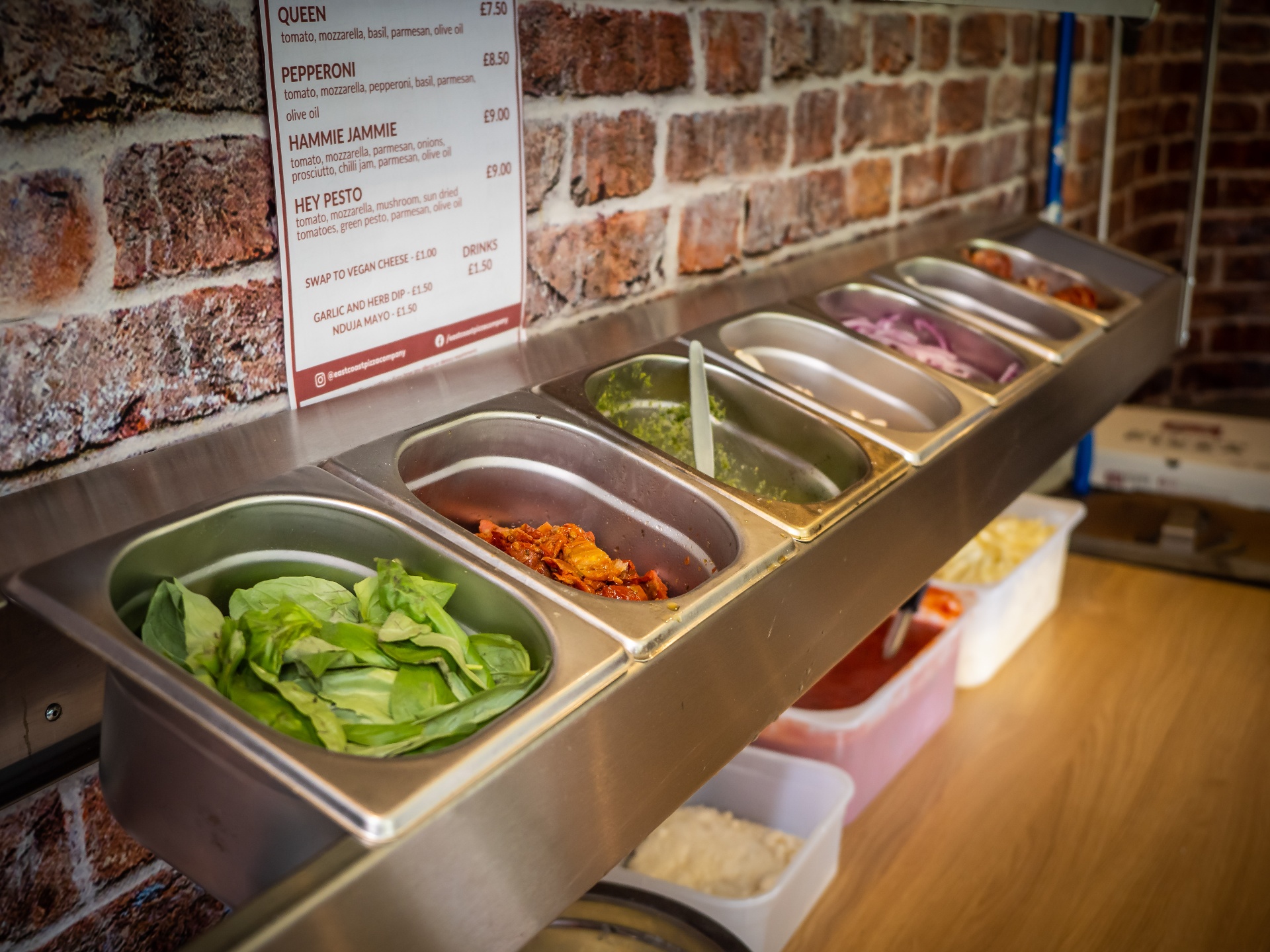 Fresh basil, nduja, pesto, red onions and toppings laid out at the Nag Box prep bar with the menu behind