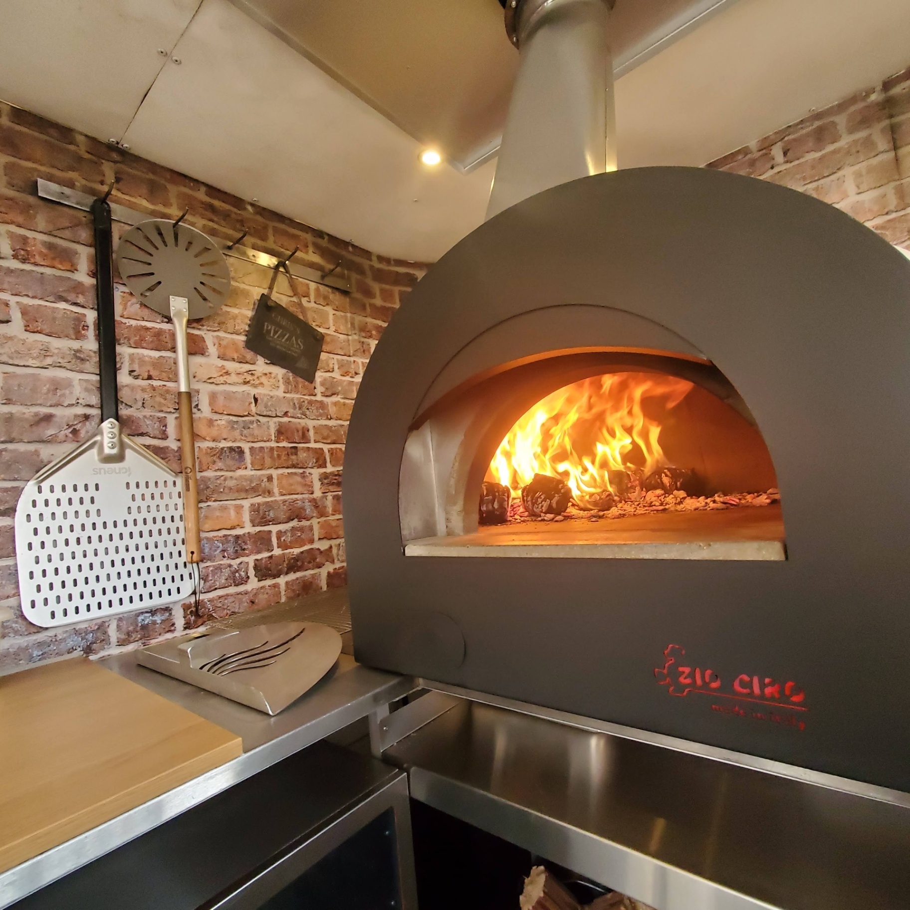 Flames roaring inside the wood-fired oven with the pizza peel beside it