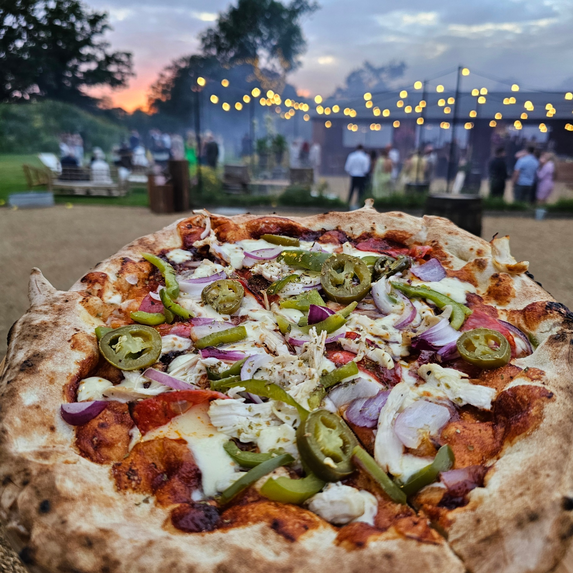 Wood-fired pizza at a sunset wedding with festoon lights and guests