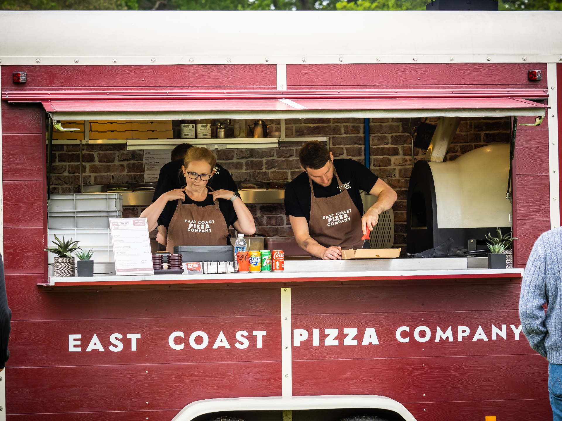 Two team members serving from the Nag Box hatch with the East Coast Pizza Company name across the front