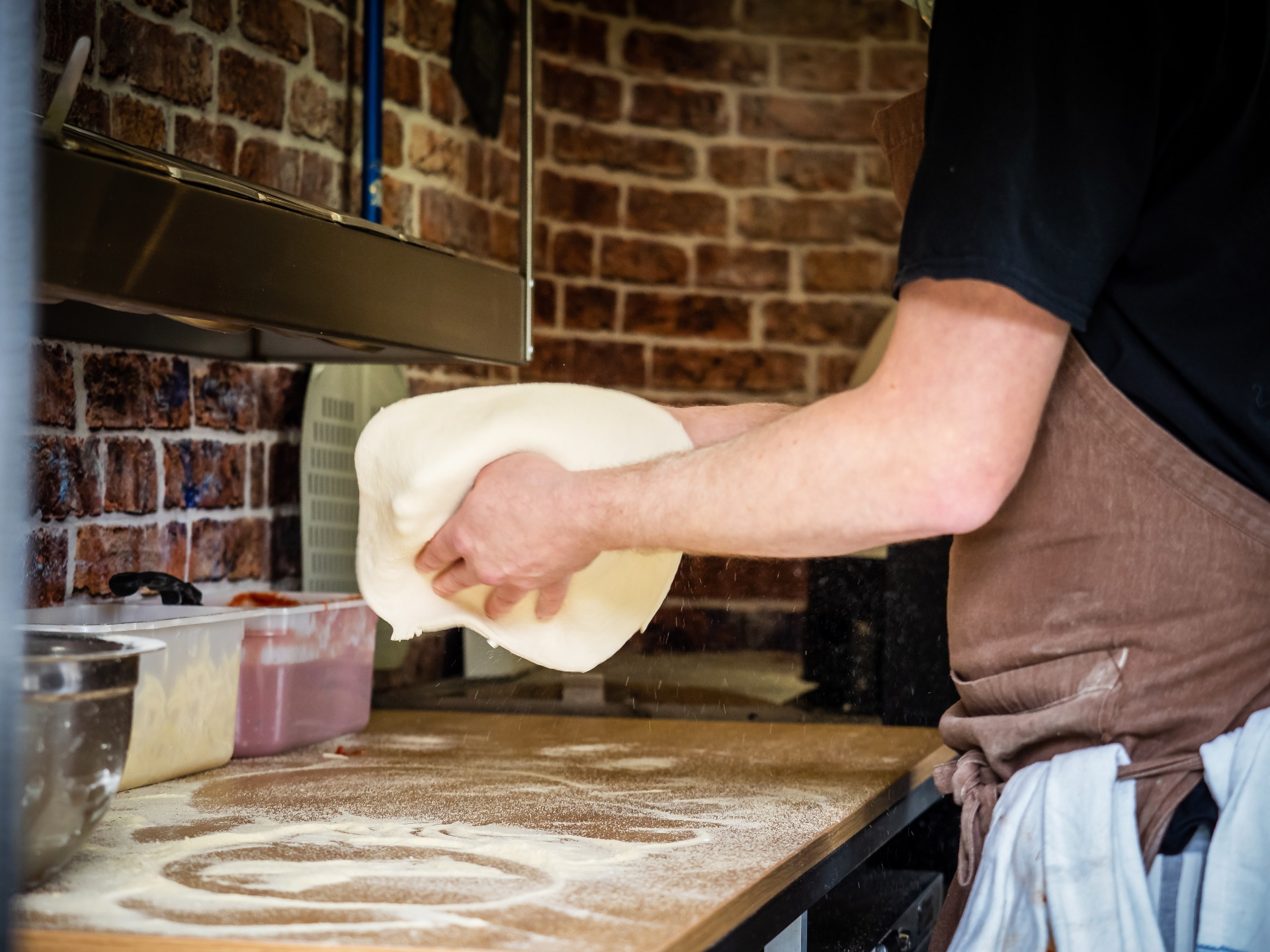 Hands stretching a dough ball on a floured counter